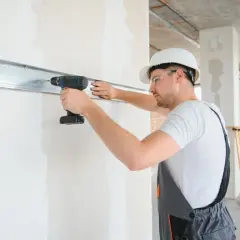 Budowlaniec w kasku przykręca metalową listwę do ściany. To kluczowy etap prac, który decyduje, czy listwy podtynkowe się zostawia.