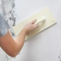 Nakładanie podkładu pod tynk mozaikowy na ścianę za pomocą kielni.