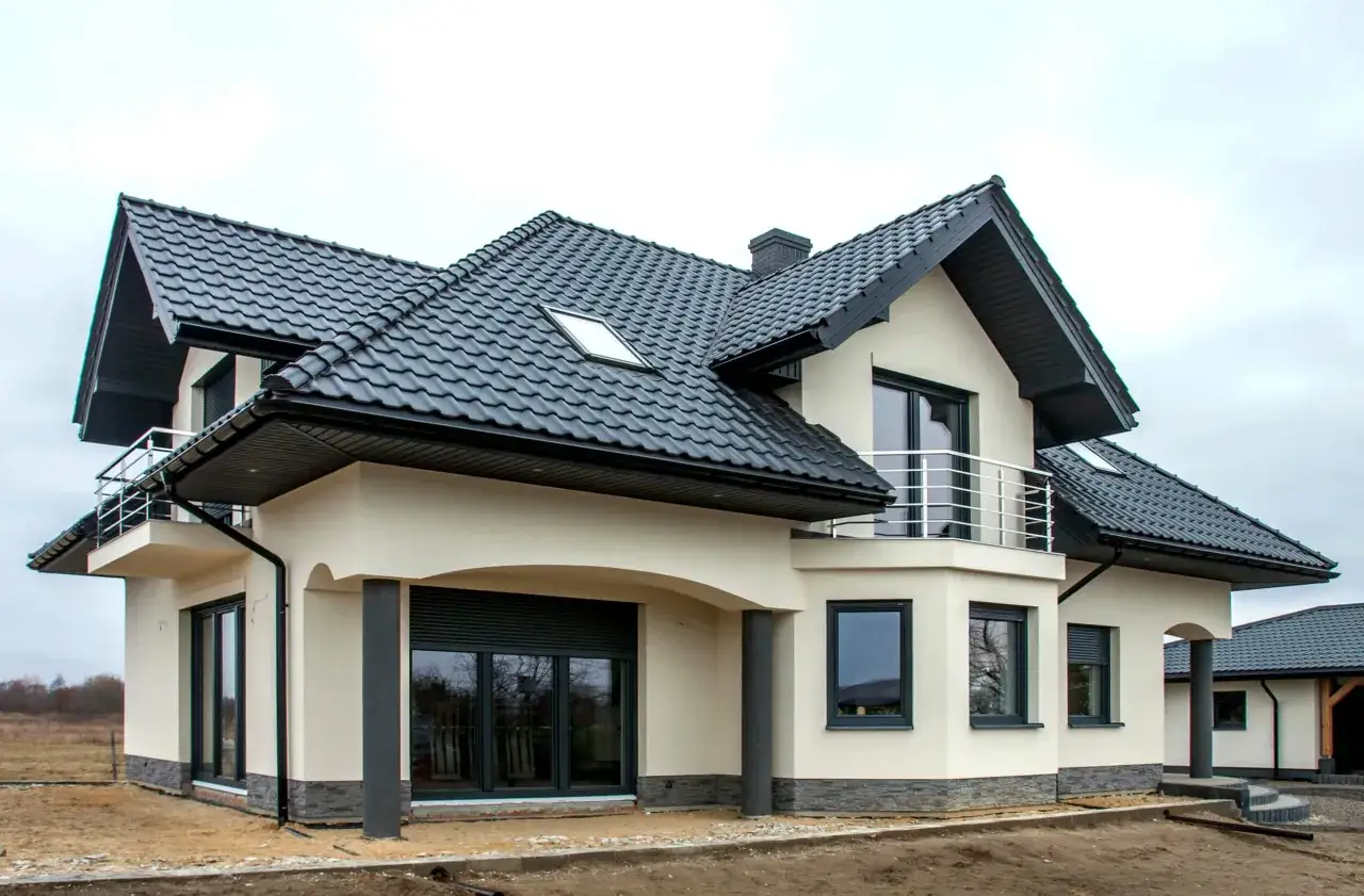 Nowy dom z jasnym tynkiem do elewacji, czarnym dachem i nowoczesnymi oknami.